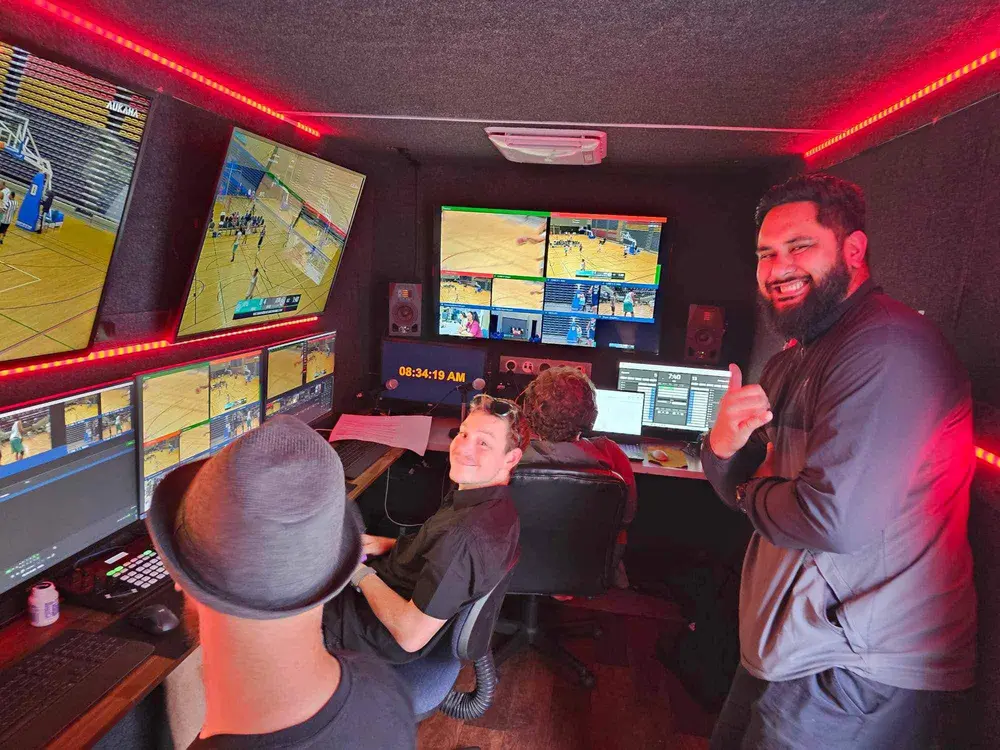Crew inside the OB truck producing a live basketball broadcast, with game feeds and score graphics on the monitors