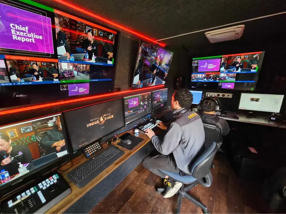 Operator at the vision switcher inside the Manaia Go OB truck, surrounded by multiview monitors during a live AGM broadcast