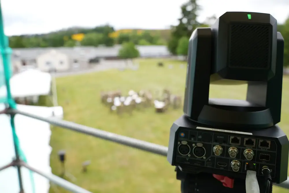 Remote-controlled PTZ broadcast camera on scaffolding overlooking an outdoor parade ground