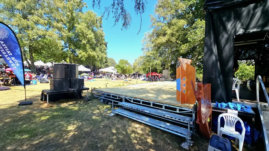 Outdoor stage and sound system at Tūwharetoa Ahurei 2025, with a large crowd under the trees